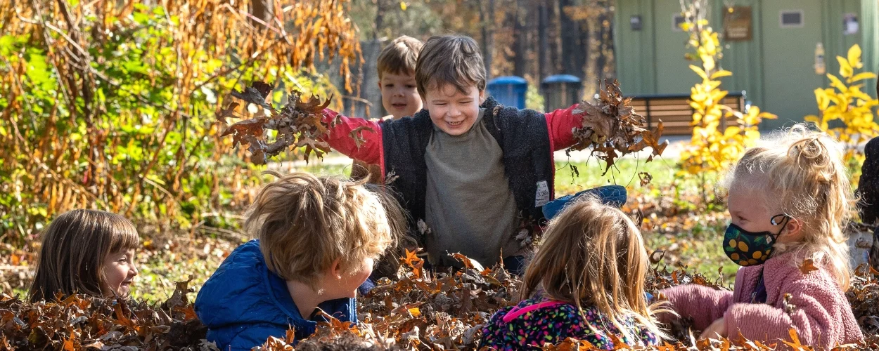 Preschool children playing in a pile of fall leaves