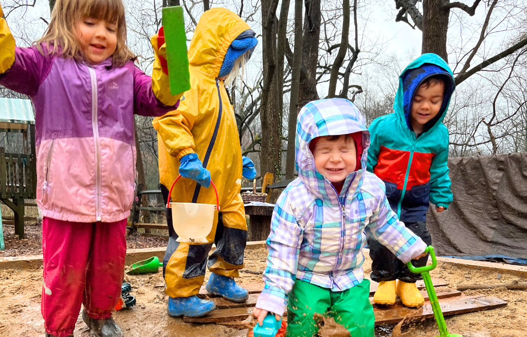 Four preschool children playing outside in puddles of water