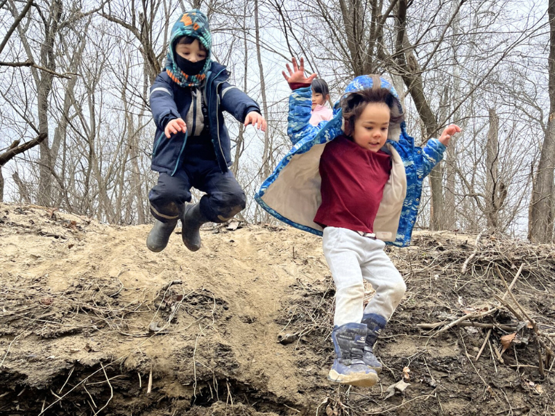 Two preschoolers dressed in winter clothes jumping into a pile of sand