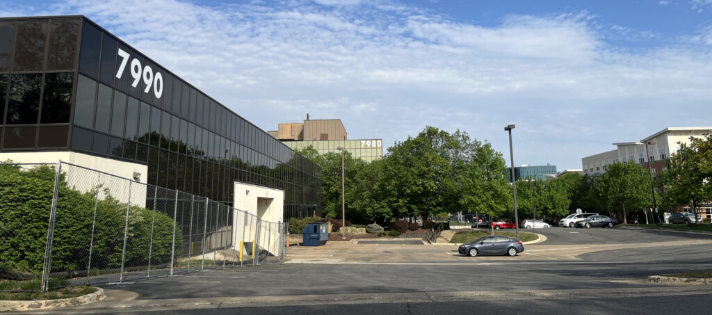 2026 photo of proposed site of Vienna Cloud in Tysons Corner, VA (Quantum Drive) with a parking lot, the current data center in the foreground, and the taller office building behind.