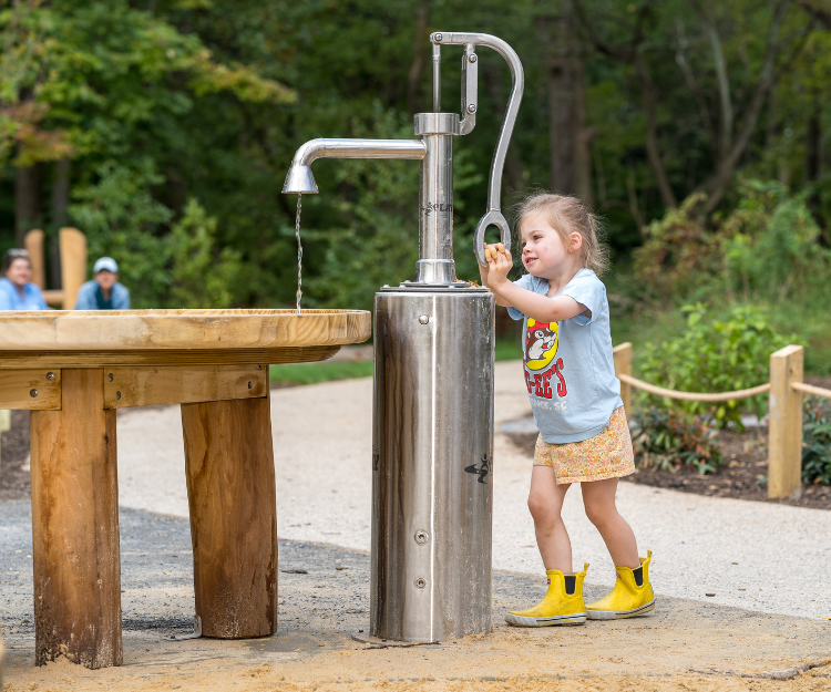 A child playing at the water pump at the Nature Play Space at Woodend Nature Sanctuary